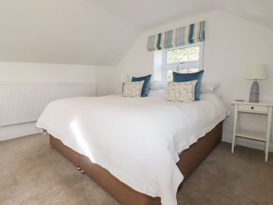 A bedroom with a large bed with white bedding and decorative pillows beside a window with striped blinds at Great Meadow Barn Crantock
