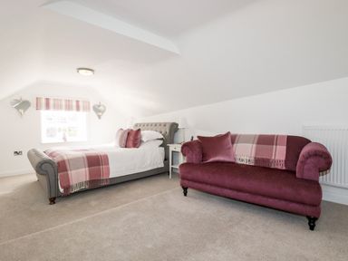 A bedroom with a bed a bedside table and a sofa with cushions and throws at Great Meadow Barn Crantock