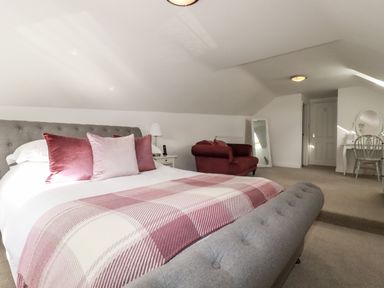 A bedroom with a bed with quilt and cushions a red upholstered sofa a full length mirror and a dressing table with chair at Great Meadow Barn in Crantock