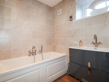 A bathroom with a bathtub and a sink with a cabinet under a window at Great Meadow Barn in Crantock