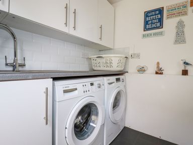 A laundry room with a sink countertop above a washing machine and dryer and wall decorations at Great Meadow Barn in Crantock