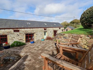 An outdoor patio area with wooden chairs potted plants and stone building at Great Meadow Barn in Crantock