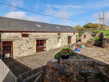 A stone barn with multiple windows and doors and a paved patio area with flower pots at Great Meadow Barn in Crantock