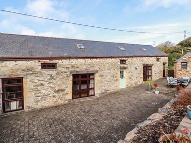 An outdoor patio area with stone paving and stone buildings with multiple windows and doors at Great Meadow Barn in Crantock