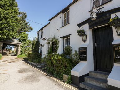 Exterior of a white building with black door and windows next to a road with plants and signs for Old Albion Inn at Great Meadow Barn in Crantock