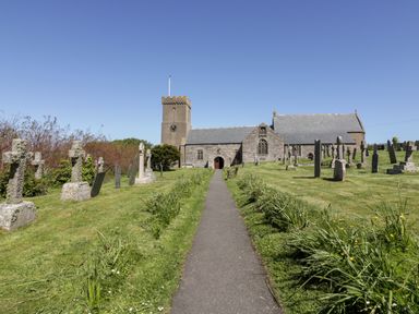 A pathway leading to a stone church with a clock tower surrounded by gravestones and grass