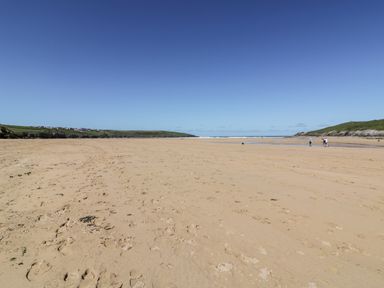 A wide sandy beach with footprints hills on both sides and a few people walking near the water at Great Meadow Barn in Crantock