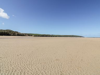 A sandy beach with a grassy cliff and houses in the distance at Great Meadow Barn in Crantock