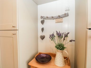A corner with a wooden table holding a cream jug with flowers and a dark bowl with cabinets on either side at Hollytree Lodge Beckside 1 Limefitt Park near Windermere