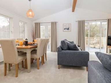 A dining area with a wooden table and beige chairs next to a living room with blue sofas at Hollytree Lodge Beckside 1 Limefitt Park near Windermere