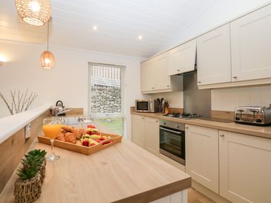 A kitchen with wooden countertops a tray of croissants and fruit a glass of orange juice a microwave an oven and toaster at Hollytree Lodge Beckside 1 Limefitt Park near Windermere