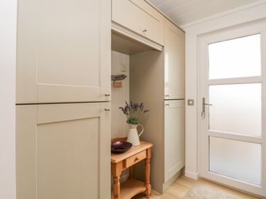 A small wooden table with a vase of flowers and a bowl between kitchen cabinets near a frosted glass door at Hollytree Lodge Beckside 1 Limefitt Park near Windermere