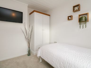 A bedroom with a white wardrobe bed a wall-mounted television and decorative wall shelves at Hollytree Lodge Beckside 1 Limefitt Park near Windermere