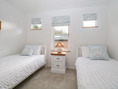 A bedroom with two single beds a nightstand with a lamp and three small windows at Hollytree Lodge Beckside 1 Limefitt Park near Windermere