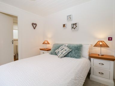 A bedroom with a double bed two bedside tables with lamps and decorative wall shelves at Hollytree Lodge Beckside 1 Limefitt Park near Windermere
