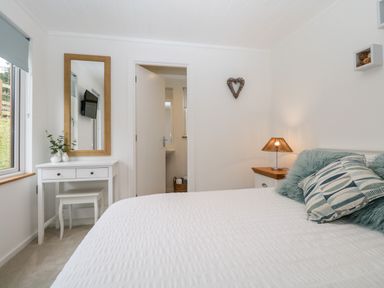 A bedroom with a white bed a bedside table with a lamp a dressing table with a mirror and a window at Hollytree Lodge Beckside 1 Limefitt Park near Windermere