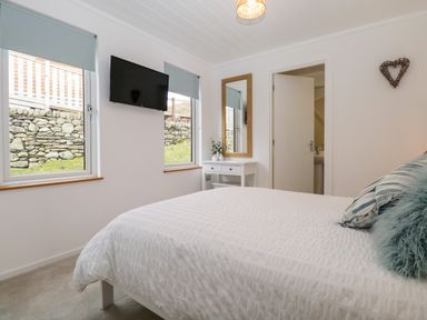 A bedroom with a bed white bedding pillows and a TV on the wall at Hollytree Lodge Beckside 1 Limefitt Park near Windermere