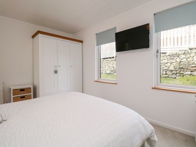 A bedroom with a white bed a white wardrobe a small white chest of drawers and a wall mounted television at Hollytree Lodge Beckside 1 Limefitt Park near Windermere
