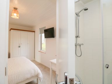 A bedroom with a wardrobe a bed a wall-mounted TV and a shower visible through a partially open door at Hollytree Lodge Beckside 1 Limefitt Park near Windermere