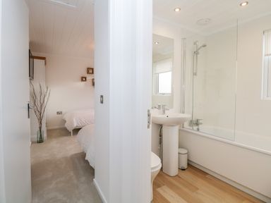 A bedroom with two beds and a bathroom with a bathtub and sink at Hollytree Lodge Beckside 1 Limefitt Park near Windermere
