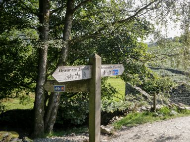 A wooden signpost with directions to Grasmere and Ambleside on a path with trees and stone walls nearby