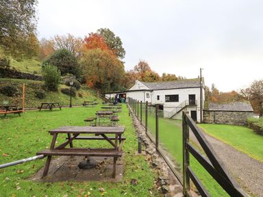 An outdoor seating area with picnic tables and a glass fence next to a white building and grass at Hollytree Lodge in Beckside 1 Limefitt Park near Windermere