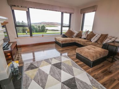 A living room with a brown sectional sofa a geometric patterned rug and large windows overlooking a landscape at Upper Killult in Killult near Gortahork County Donegal
