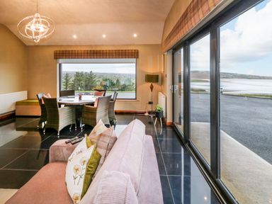 A dining area with a round table and chairs next to large windows overlooking water and countryside at Upper Killult in Killult near Gortahork County Donegal