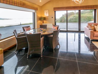 A dining area with a round glass table and wicker chairs near large windows and a sliding glass door at Upper Killult in Killult near Gortahork County Donegal