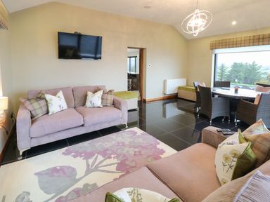 A living room with two sofas a wall-mounted TV a rug and a dining table with chairs near a large window at Upper Killult in Killult near Gortahork County Donegal