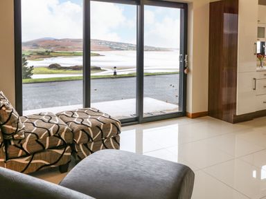 A room with patterned chairs and a large glass sliding door overlooking a coastal landscape at Upper Killult in Killult near Gortahork County Donegal