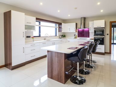 A modern kitchen with white cabinets and a large island with black bar stools at Upper Killult in Killult near Gortahork County Donegal