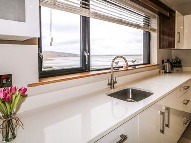 A kitchen countertop with a sink kettle and flowers by a window with a view of a beach at Upper Killult in Killult near Gortahork County Donegal