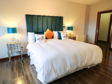 A bedroom with a large bed with a blue upholstered headboard blue lamps on bedside tables and wooden flooring at Upper Killult in Killult near Gortahork County Donegal