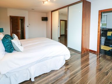 A bedroom with a large bed pillows a wall-mounted television a sliding door wardrobe and an adjoining bathroom at Upper Killult in Killult near Gortahork County Donegal