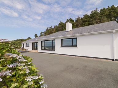 An exterior view of a white house with black window frames and a grey roof surrounded by trees and flowers at Upper Killult in Killult near Gortahork County Donegal