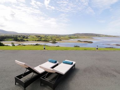 Two lounge chairs with towels on a paved area overlooking a river and green fields at Upper Killult in Killult near Gortahork County Donegal
