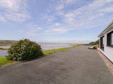 A driveway next to a white building with windows overlooking a grass area a bush a body of water and hills at Upper Killult in Killult near Gortahork County Donegal