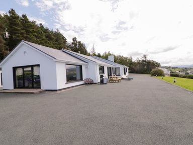 A single story house with white walls and large windows with outdoor seating and trees in the background at Upper Killult in Killult near Gortahork County Donegal