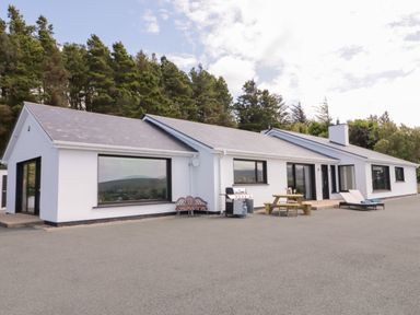 A white single-story house with large windows outdoor seating and barbecue in front at Upper Killult in Killult near Gortahork County Donegal