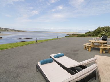 An outdoor patio with two lounge chairs with towels a round wooden picnic table and a grill near a body of water at Upper Killult in Killult near Gortahork County Donegal