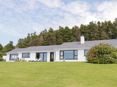 A single story house with large windows a lawn and trees in the background at Upper Killult in Killult near Gortahork County Donegal