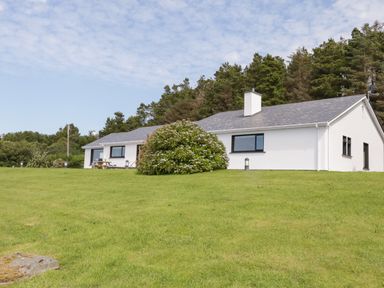 A white single-story house with a gray roof surrounded by green grass and trees at Upper Killult in Killult near Gortahork County Donegal