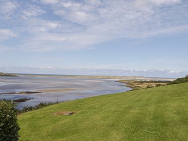 A grassy hill overlooking a wide estuary with water and sandbanks under a partly cloudy sky at Upper Killult in Killult near Gortahork County Donegal