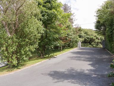 A paved driveway with trees and bushes on both sides leading to metal gates at Upper Killult in Killult near Gortahork County Donegal