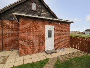 A brick building with a white door numbered 235 and a small fenced garden area at Chalet 235 in Wilsthorpe near Bridlington
