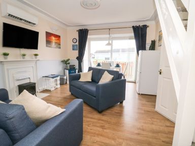 A living room with blue sofas a mounted television and a dining table near patio doors at Chalet 235 in Wilsthorpe near Bridlington