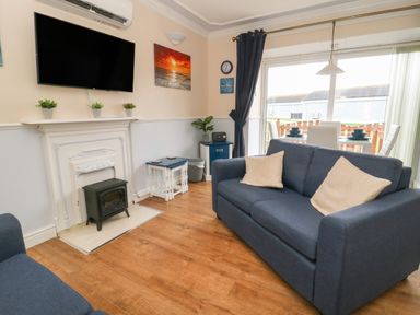 A living room with two blue sofas a TV above a fireplace and a dining table near a sliding glass door at Chalet 235 in Wilsthorpe near Bridlington