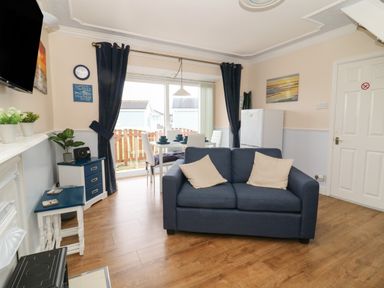 A living room with a blue sofa white dining table and chairs a small fridge and a television at Chalet 235 in Wilsthorpe near Bridlington