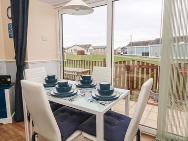 A dining area with a glass table set for four and white chairs near a sliding glass door at Chalet 235 Wilsthorpe near Bridlington